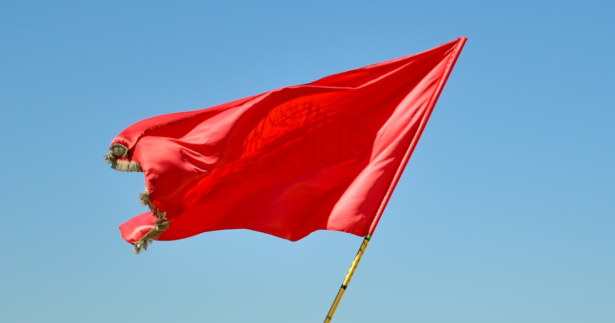 Drapeau rouge sur un mât sous un ciel bleu, symbole de signal d'alarme